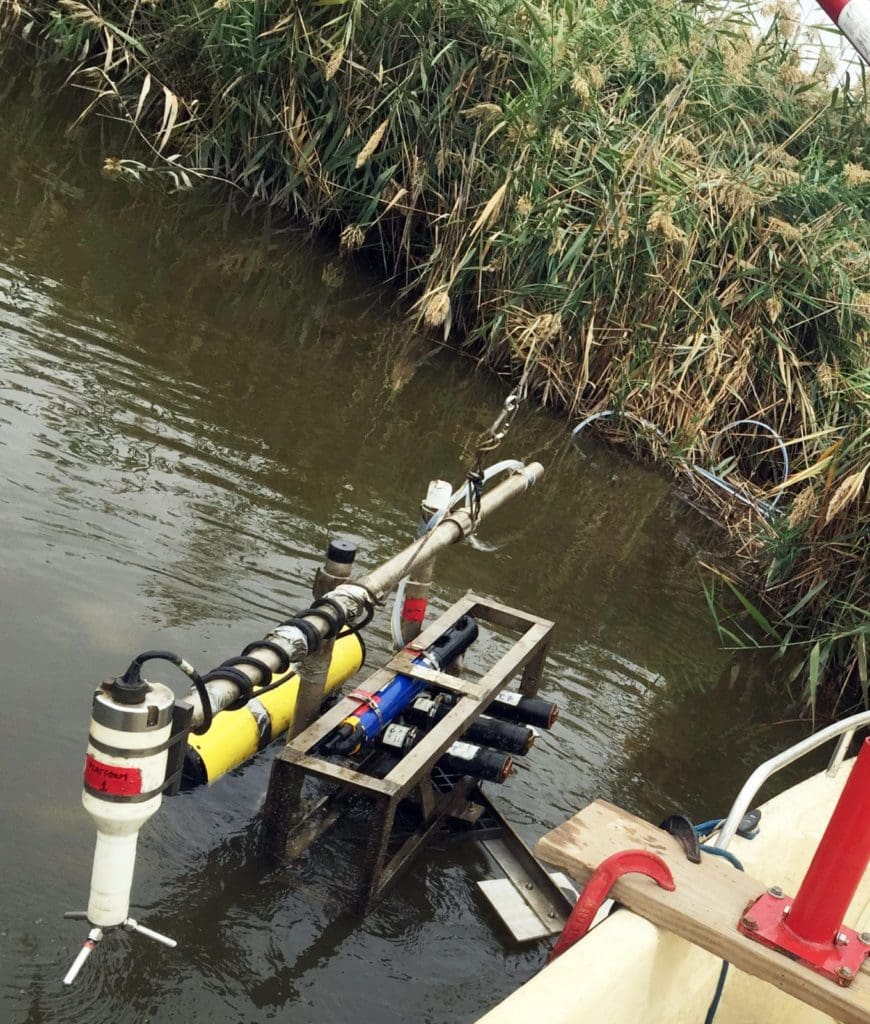 OPTICS hydrological monitoring tool deployed in wetland water near vegetation for environmental assessment.