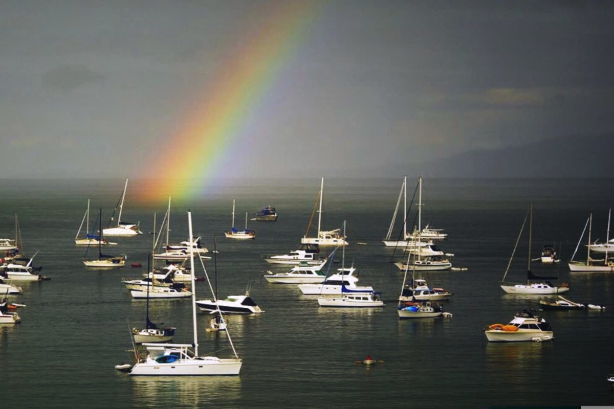 Rainbow over yachts moored in an ocean bay.